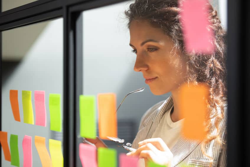 Thoughtful young female boss team leader looking at kanban board.