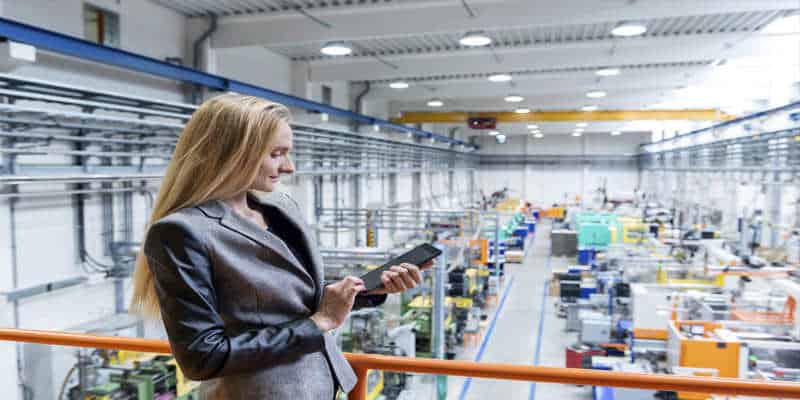 A woman in a factory looking at a Kanban software board on a tablet.