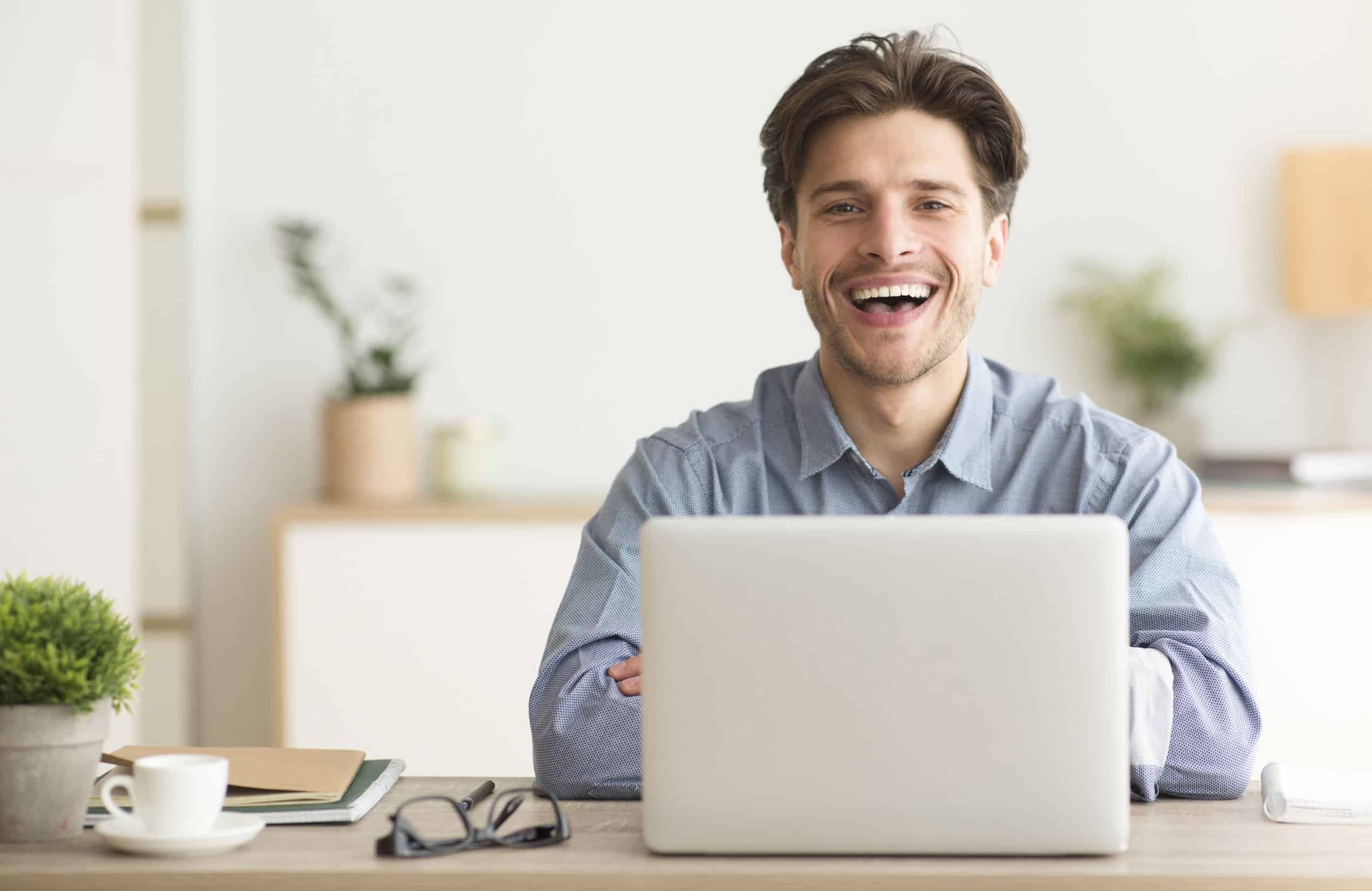 Man Sitting At Laptop And Laughing Looking At Camera